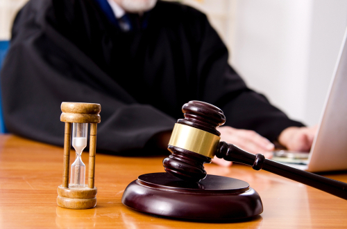 Judge’s gavel and hourglass on desk with robed attorney using laptop
