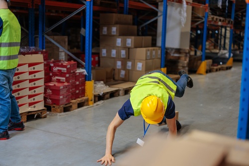 warehouse worker wearing hardhat and high-visibility vest falling on floor