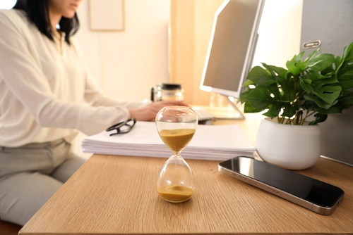 Hourglass beside smartphone on desk, illustrating waiting time or delayed communication
