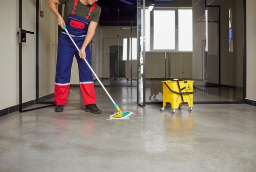 janitor in overalls mopping hallway floor beside wet floor bucket